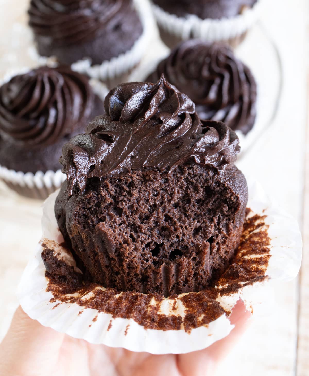 Hand holding a chocolate cupcake that has been bitten into, showing the inside.