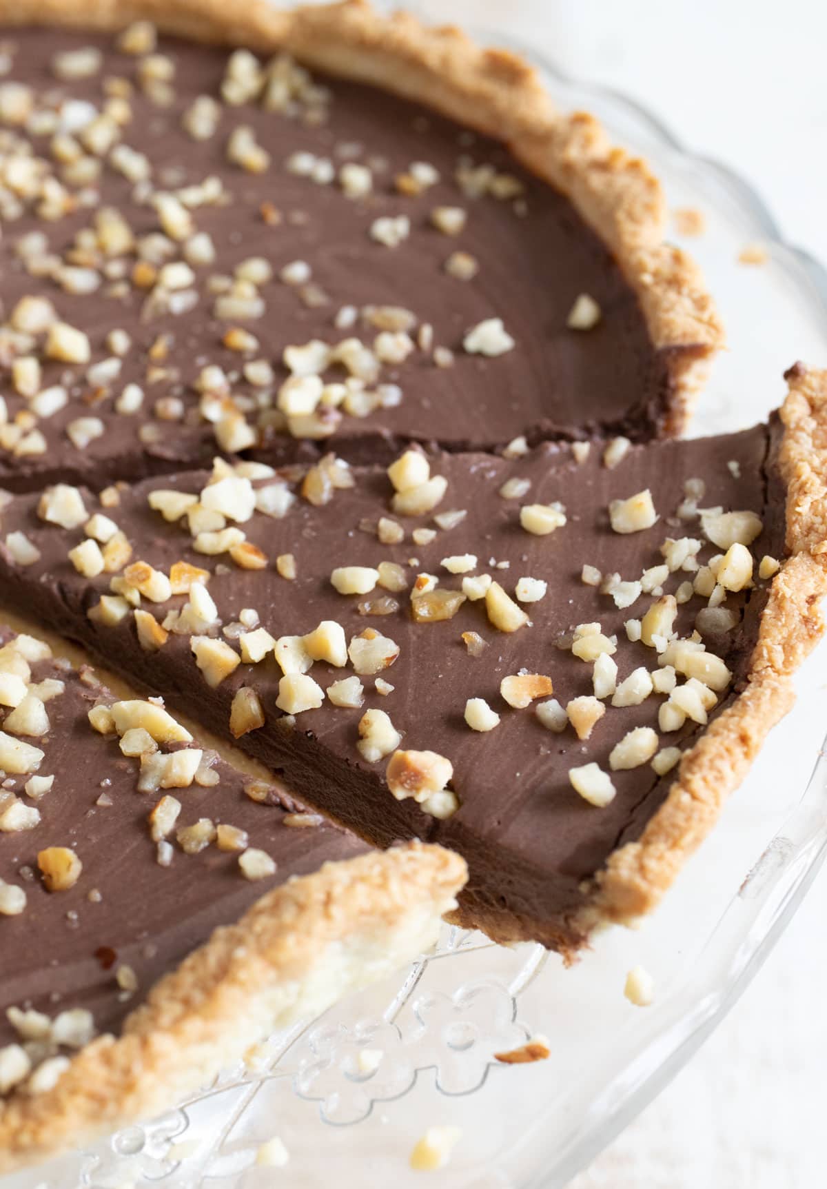 A sugar free chocolate tart topped with chopped hazelnuts on a cake stand.