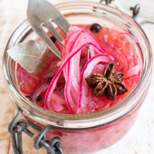 Sugar free pickled onions in a jar and a fork lifting up some of the onion slices.