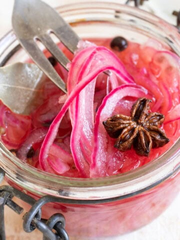 Sugar free pickled onions in a jar and a fork lifting up some of the onion slices.