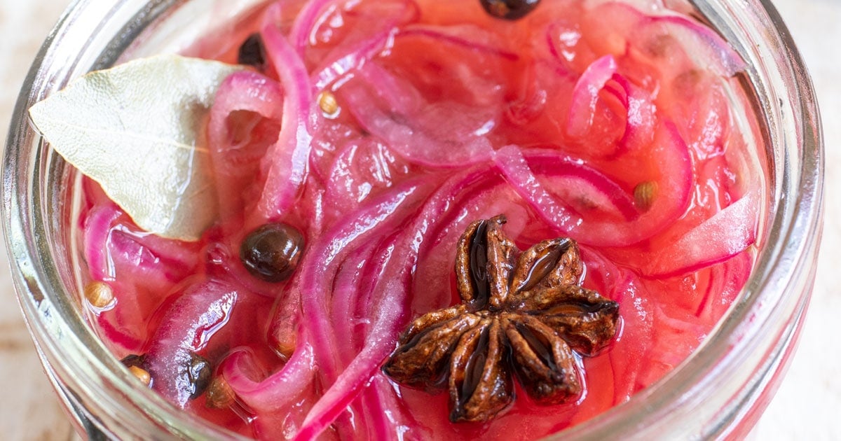 Pickled red onions and spices in a glas jar.