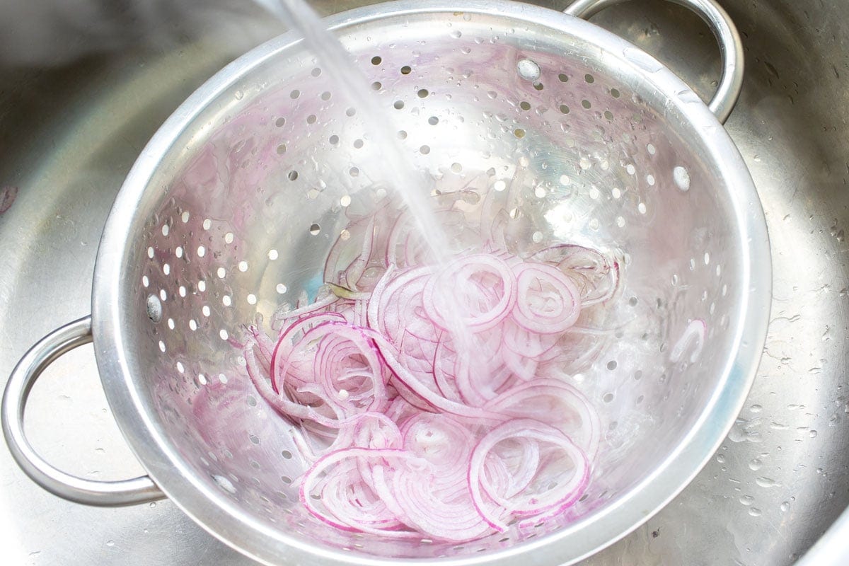 Pouring boiling water over sliced onions in a colander.