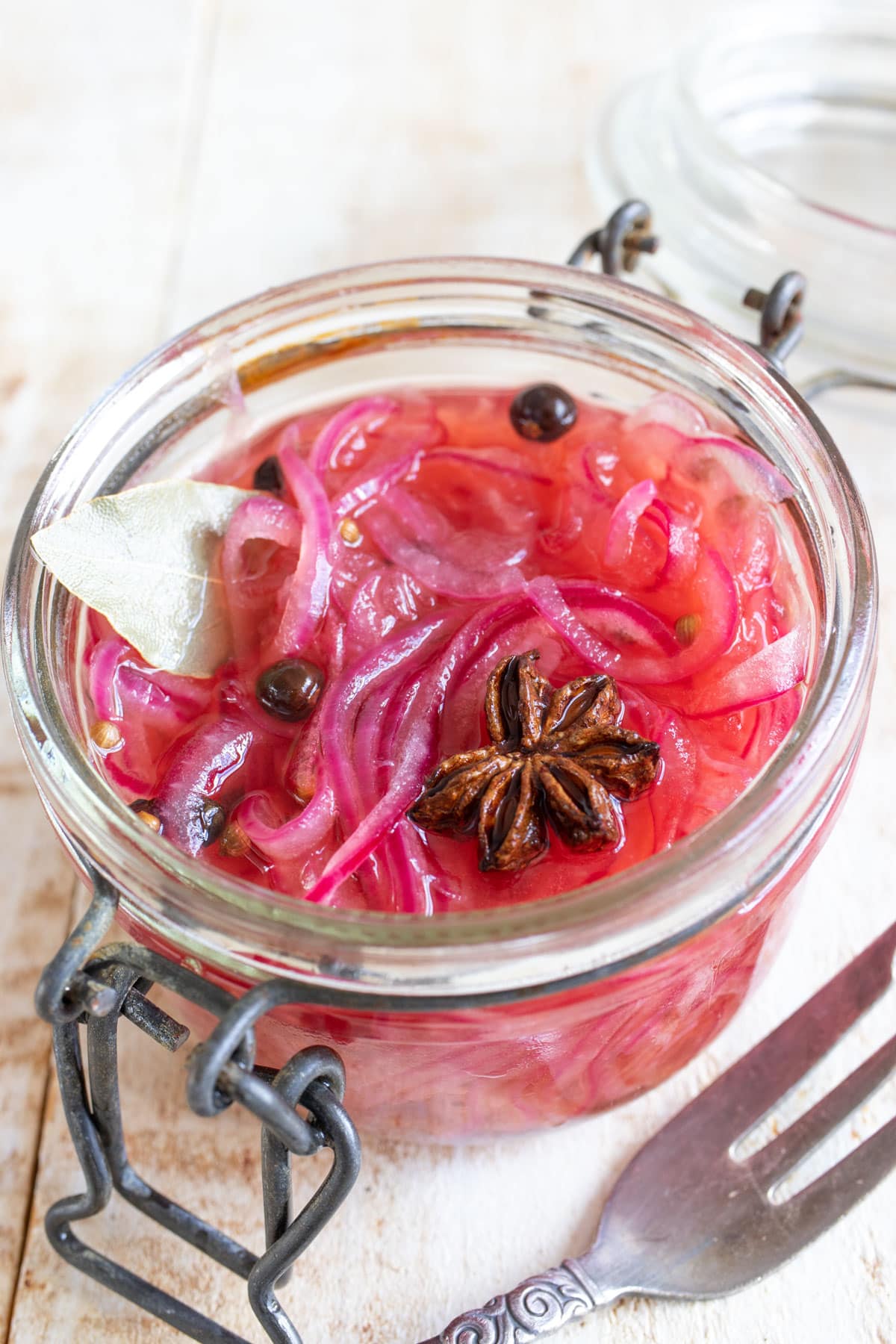 Sugar free pickled red onions in a glass jar with star anise and peppercorns.