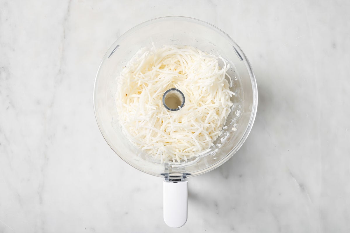 Shredded turnip in a food processor bowl.