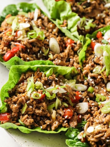 Asian pork lettuce wraps on a plate topped with spring onion.