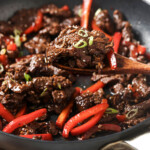 Wooden spoon lifting mongolian style beef from a pan.