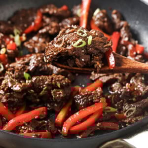 Wooden spoon lifting mongolian style beef from a pan.