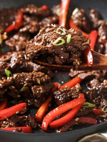 Wooden spoon lifting mongolian style beef from a pan.