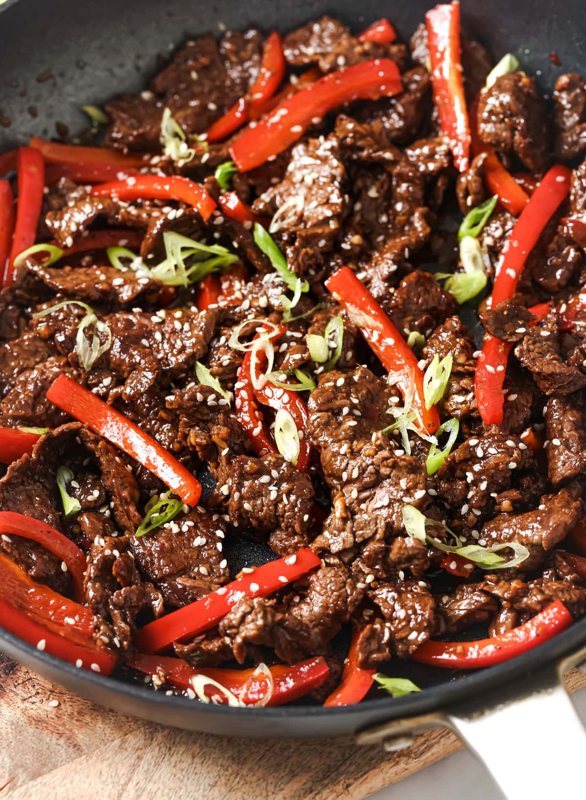 Strips of beef cooked in a soy sauce with red pepper strips in a pan.