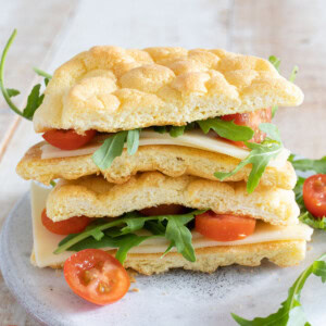 A sandwich made with cloud bread and filled with cheese and lettuce and tomato sliced, sliced open in half.
