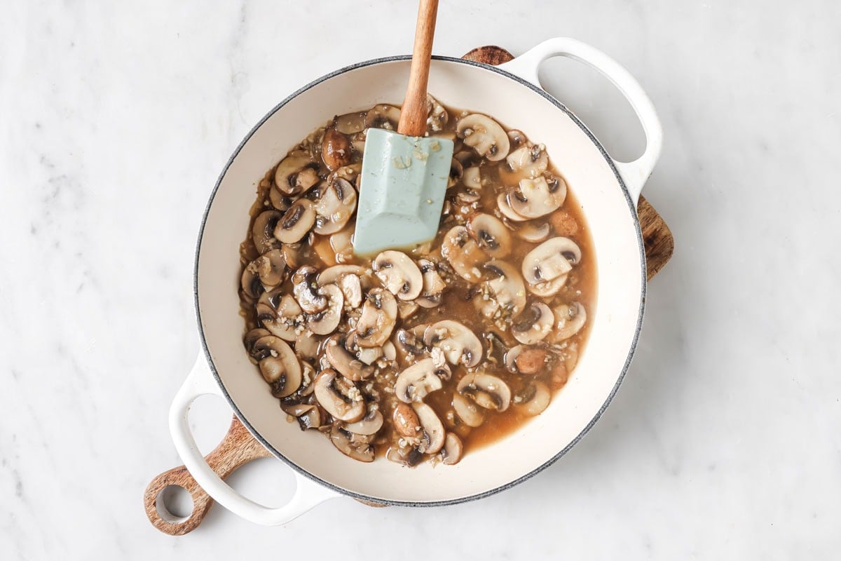 Adding broth and wine to the sliced mushrooms.