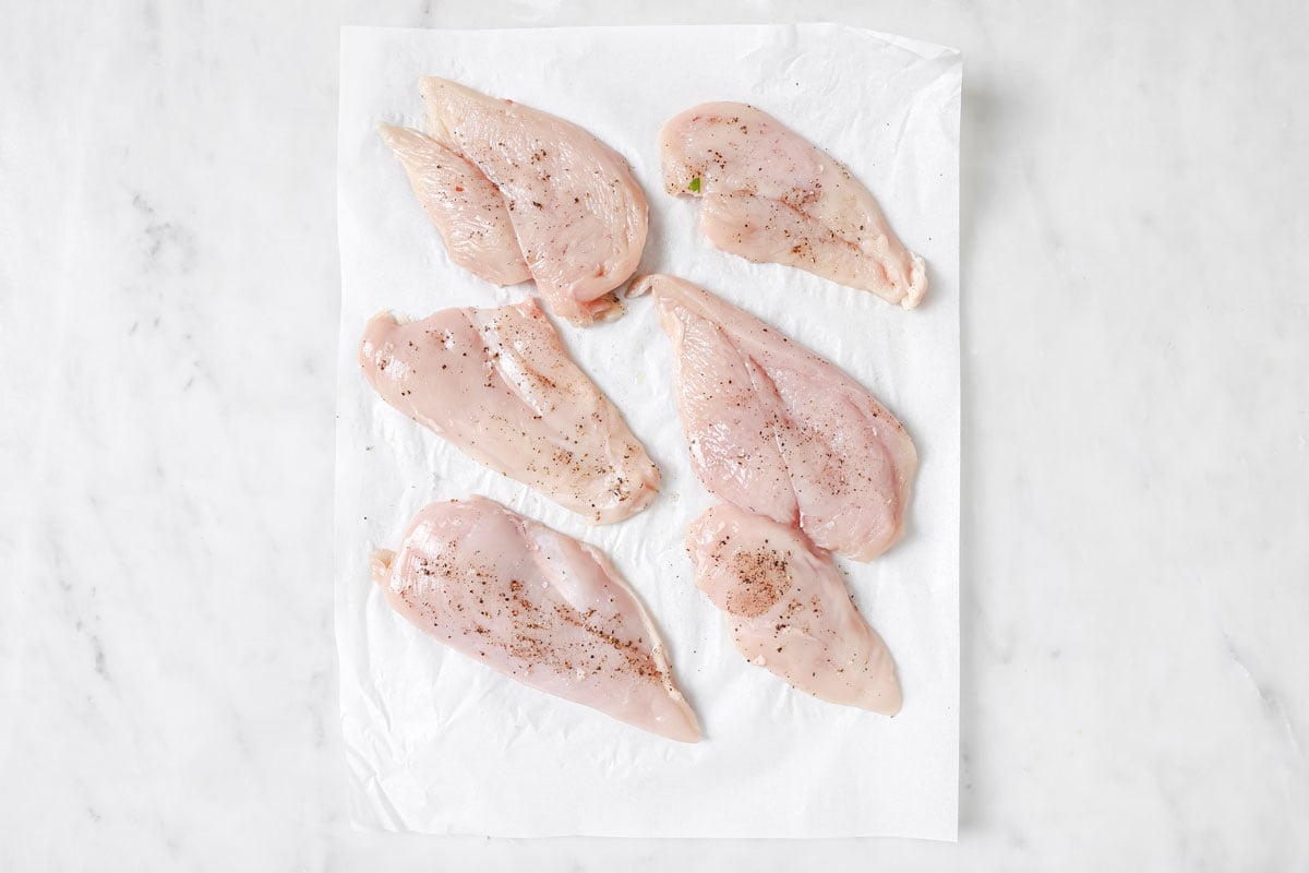 Seasoned raw chicken fillets on a sheet or parchment paper.