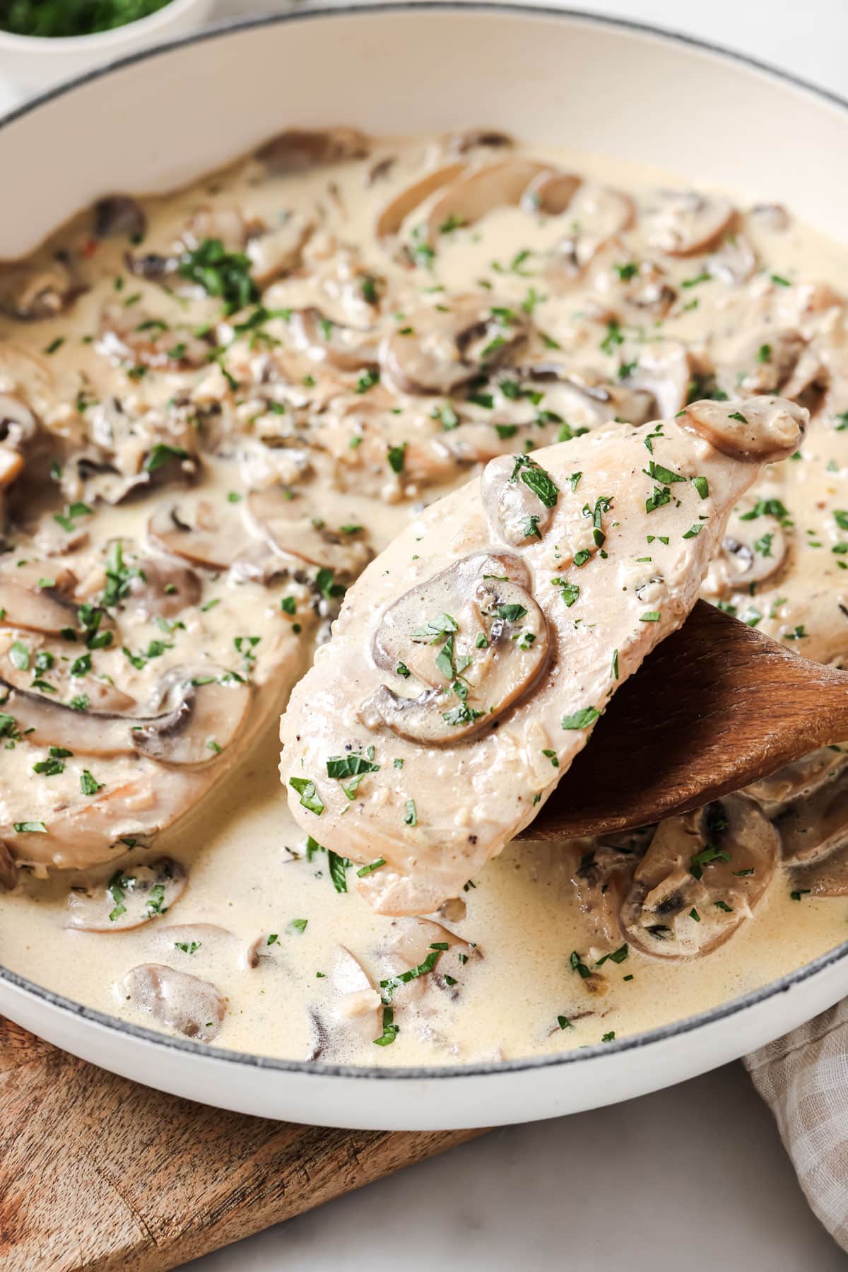 Wooden spoon lifting a cooked chicken fillet.