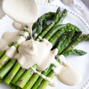 Drizzling the tonnato sauce over steamed asparagus.