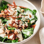 A warm kale salad with crisped ham, chopped nuts, parmesan and tahini dressing on a plate.