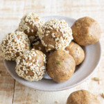 A bowl with peanut butter energy balls, some are rolled in toasted sesame seeds.