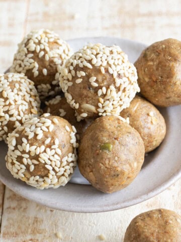 A bowl with peanut butter energy balls, some are rolled in toasted sesame seeds.