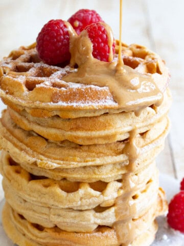 A stack of protein waffles with peanut butter drizzle and raspberries.