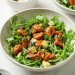 A plate with shrimp avocado salad made with rocket, spicy fried shrimp, cubed avocado and seeds.
