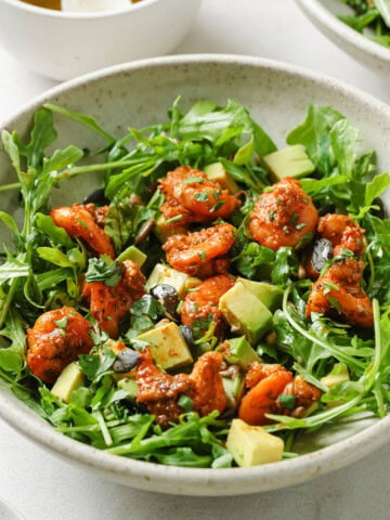 A plate with shrimp avocado salad made with rocket, spicy fried shrimp, cubed avocado and seeds.