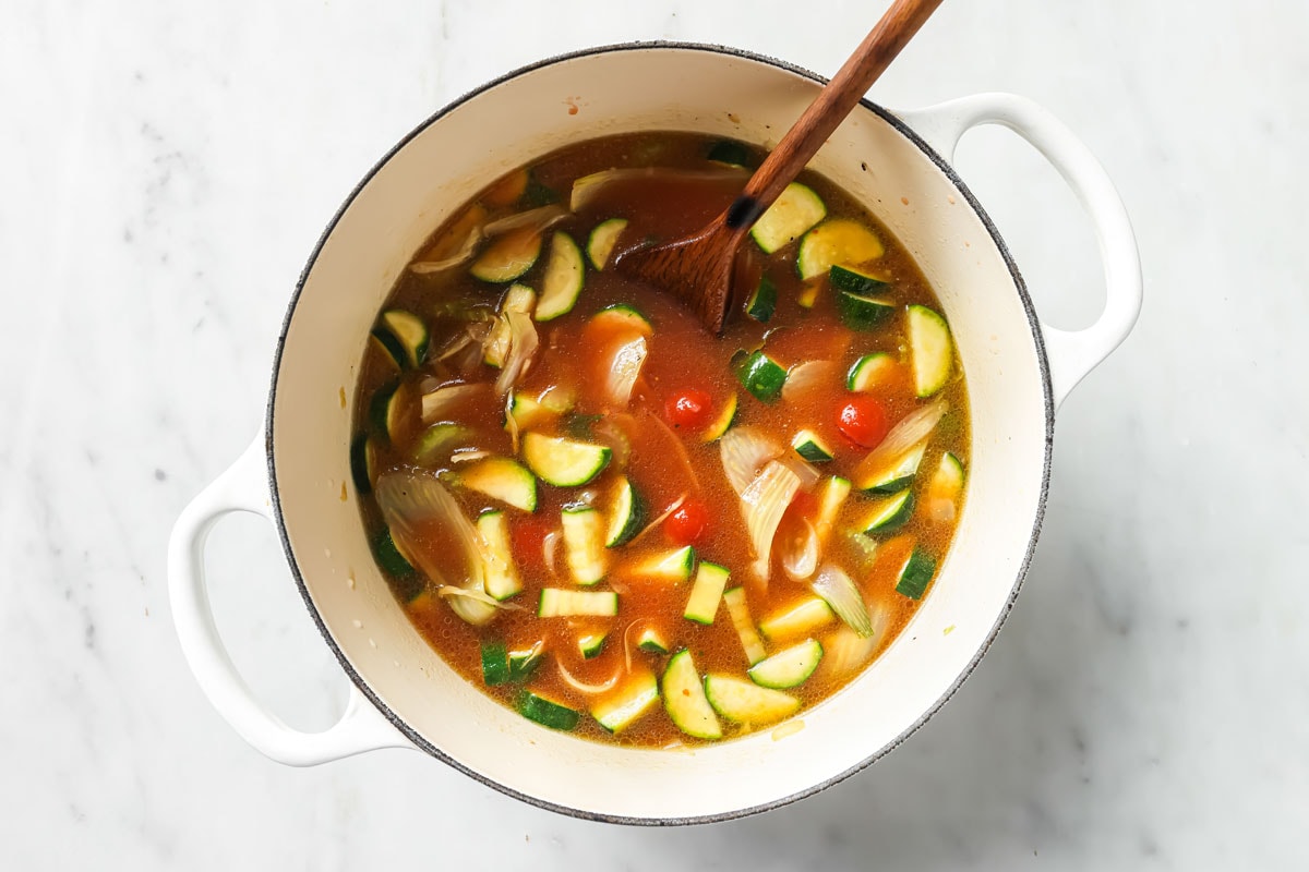 Adding the soup stock and canned cherry tomatoes to the zucchini and vegetables.