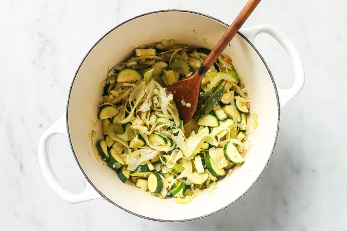 Adding the sliced zucchini into the pot with sauteed vegetables.