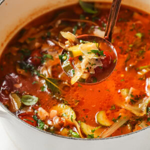 A ladle with zucchini soup above a large pot of soup.