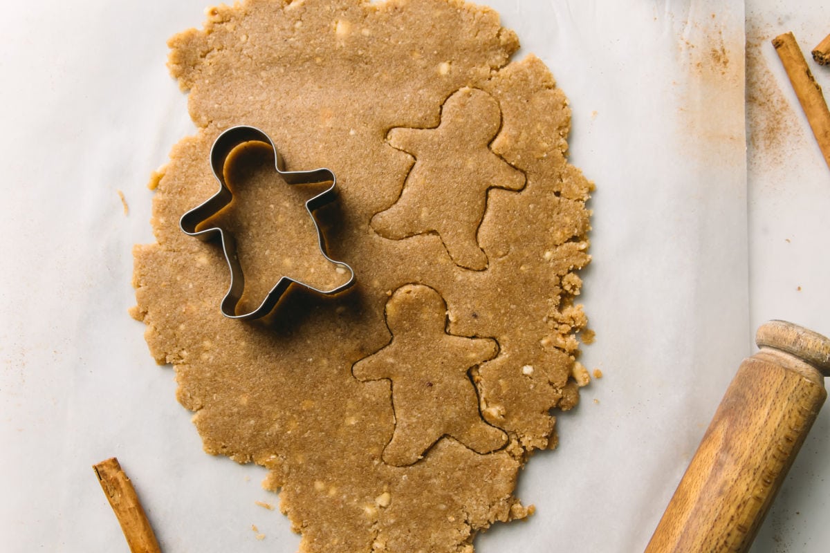 Rolled out cookie dough and a gingerbead man cookie cutter making shapes.