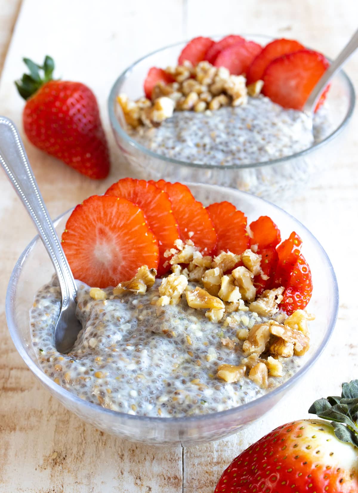 Chia porridge in 2 bowls topped with sliced strawberries and walnuts.