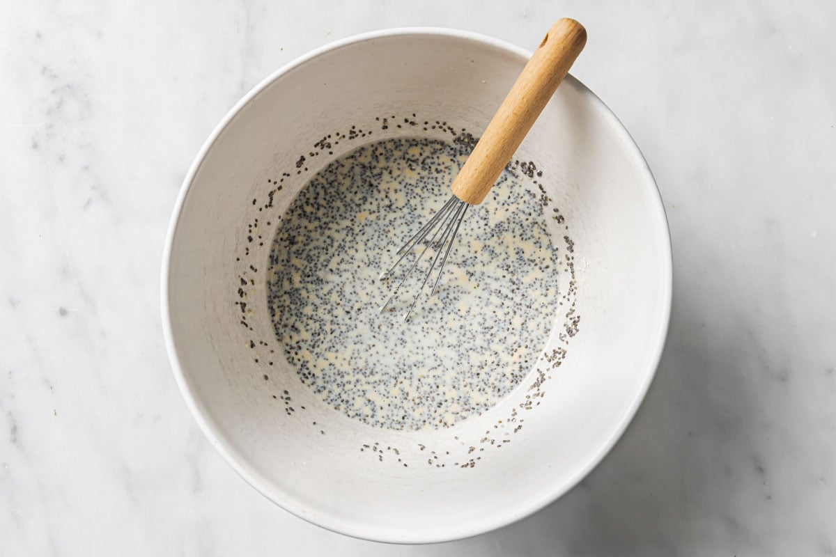 Mixing chia seeds with whey protein powder and soy milk in a bowl with a balloon whisk.