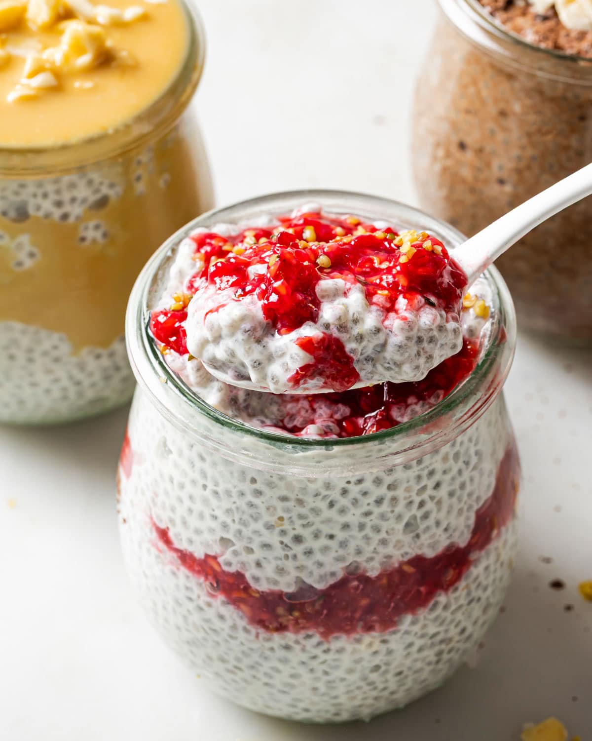 Protein chia pudding in a jar with raspberry sauce and a spoon.