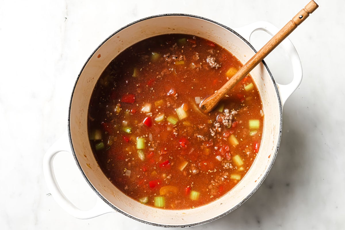 Adding broth, tomato paste and chopped tomatoes to the sautéed chopped peppers and vegetables.