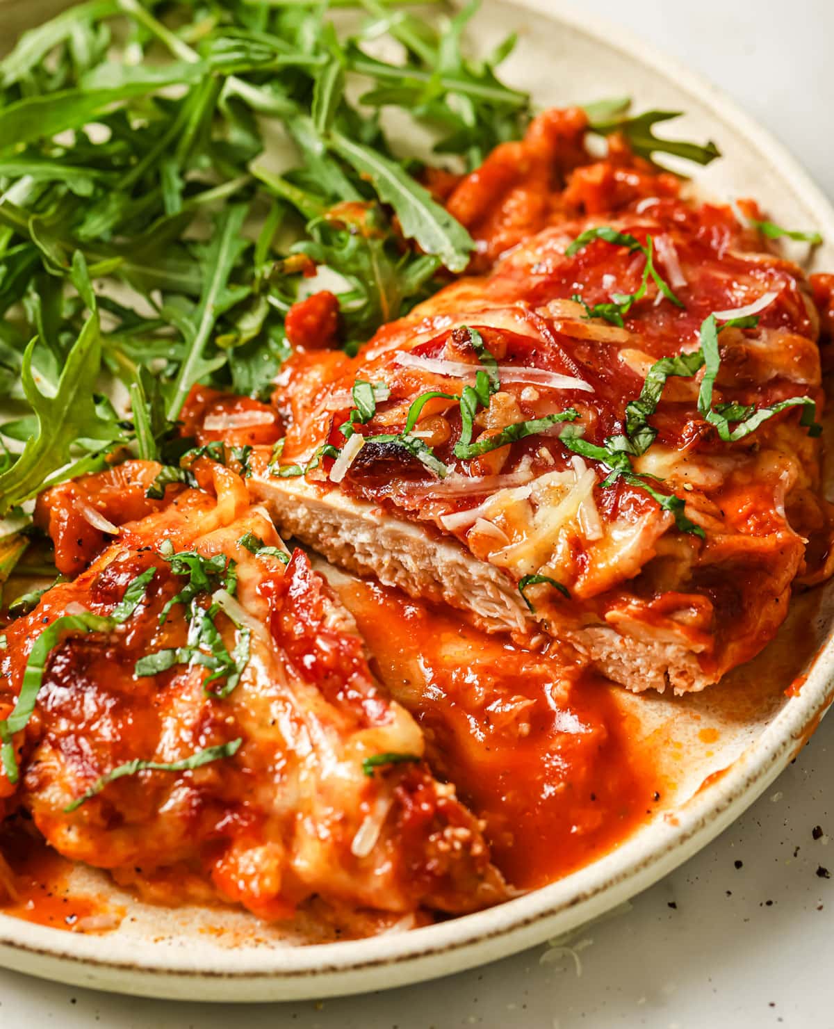 A pizza chicken fillet on a plate, sliced in half and served with lettuce.