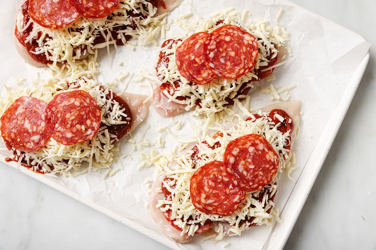 Adding shredded mozzarella and salami onto the chicken fillets.