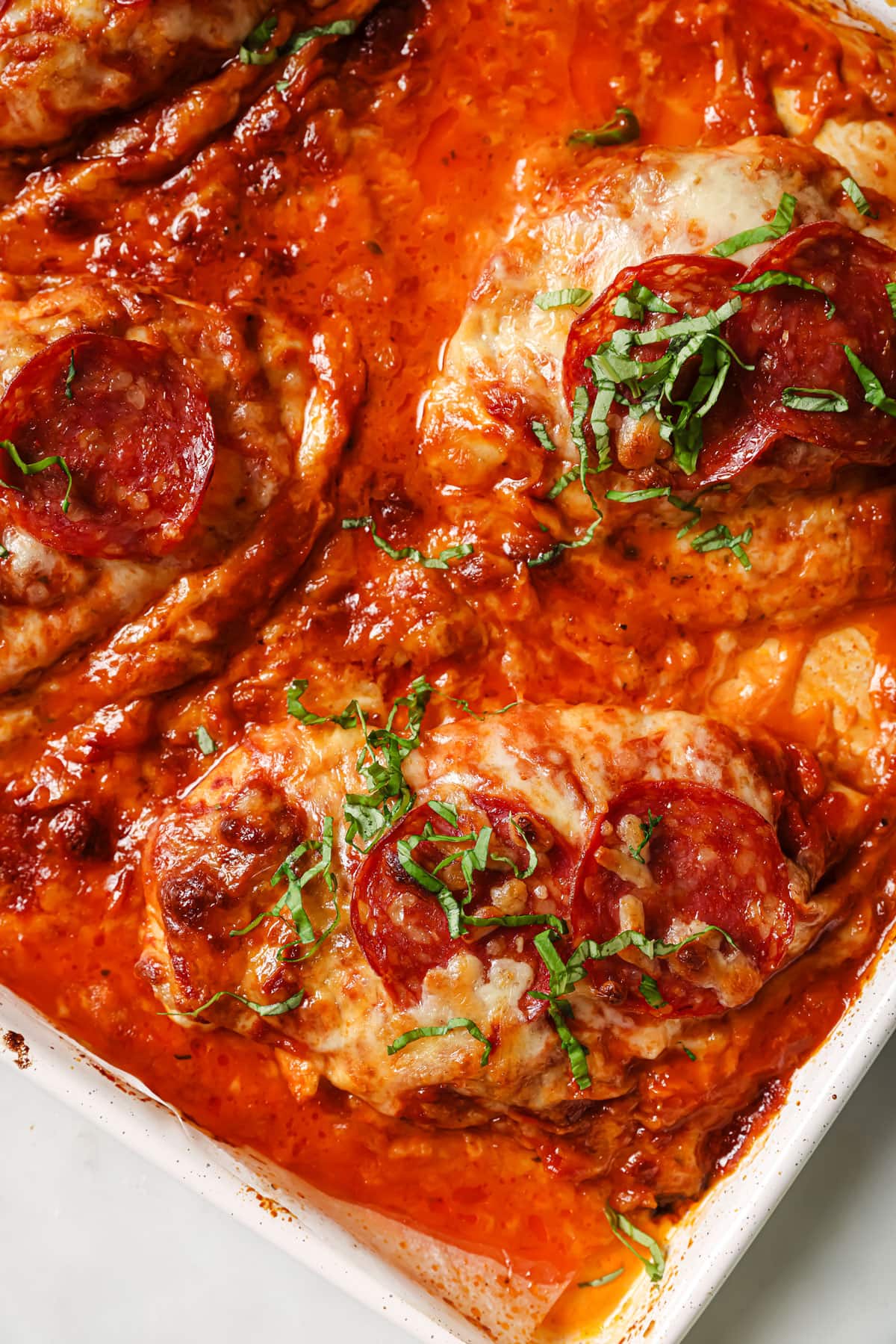 Pizza chicken in a casserole dish - chicken fillets topped with tomato sauce, cheese and salami..