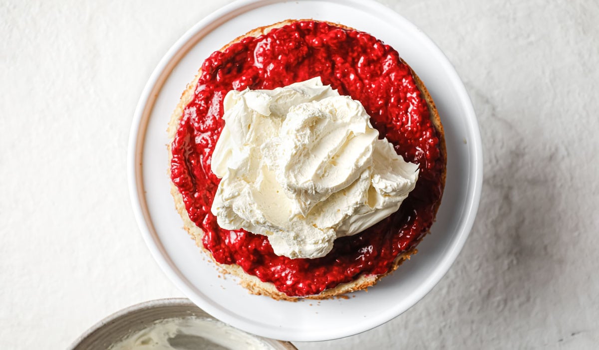 Adding whipped cream onto the raspberry jam layer.