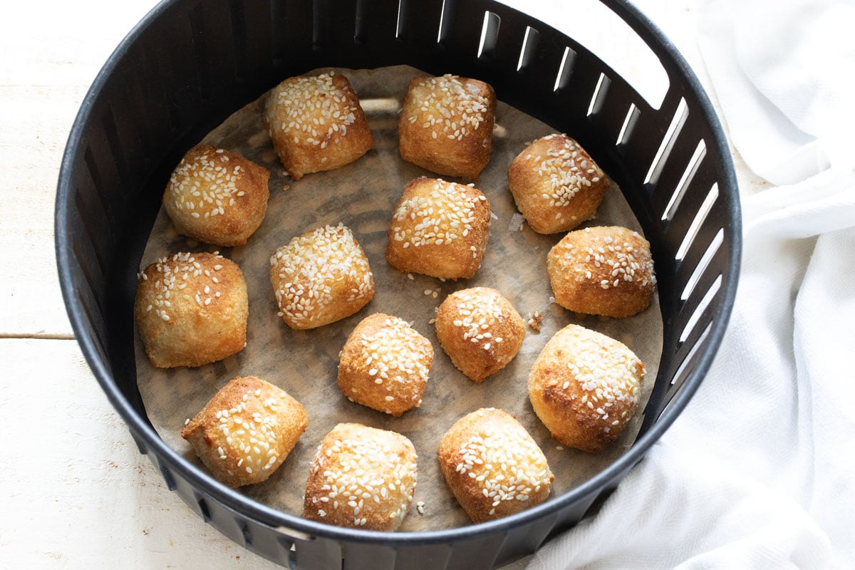 Keto pretzel bites in an air fryer basket, topped with sesame seeds.