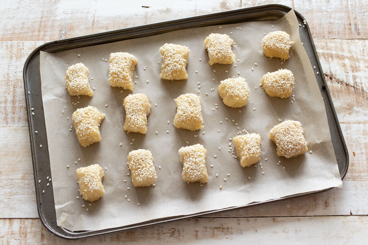 Fathead dough segments dipped in sesame seeds on a baking tray.
