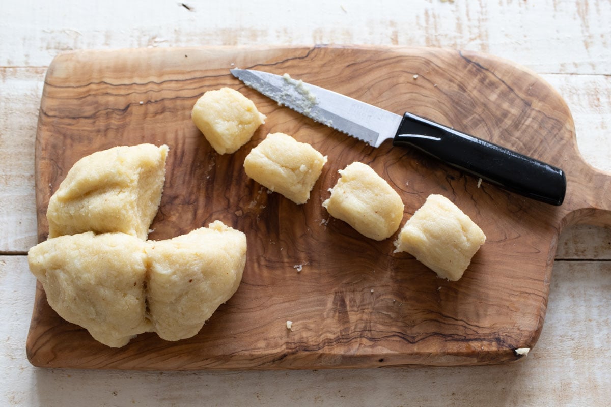 Slicing the dough log into 4 bites on a board with a knife.
