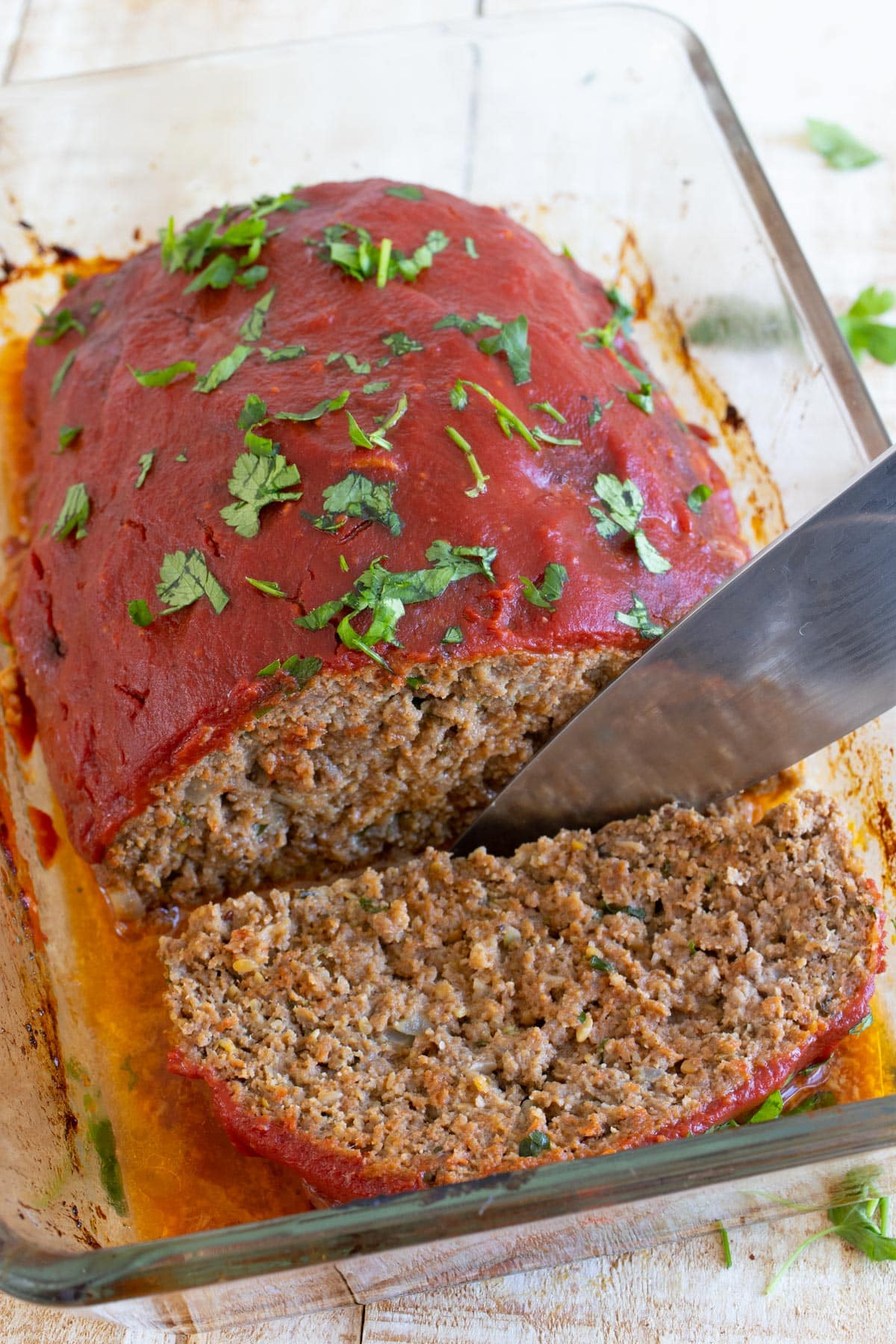 Keto meatloaf in a casserole topped with sugar free ketchup glaze being slice dwith a knife.