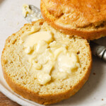 A keto mug bread with flaxseed sliced in half and spread with butter on a plate with a knife.