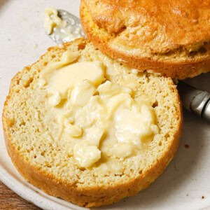 A keto mug bread with flaxseed sliced in half and spread with butter on a plate with a knife.