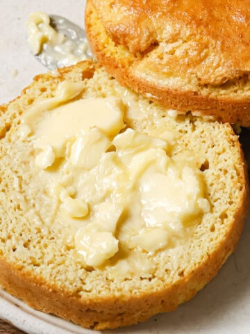 A keto mug bread with flaxseed sliced in half and spread with butter on a plate with a knife.