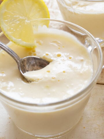 A dessert cup with keto lemon posset decorated with a lemon slice and a spoon.