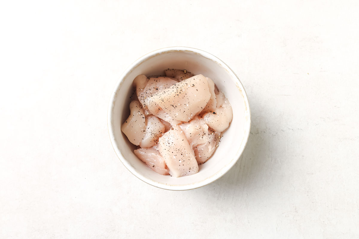 Raw chicken breast cubes seasoned with salt and pepper in a bowl.