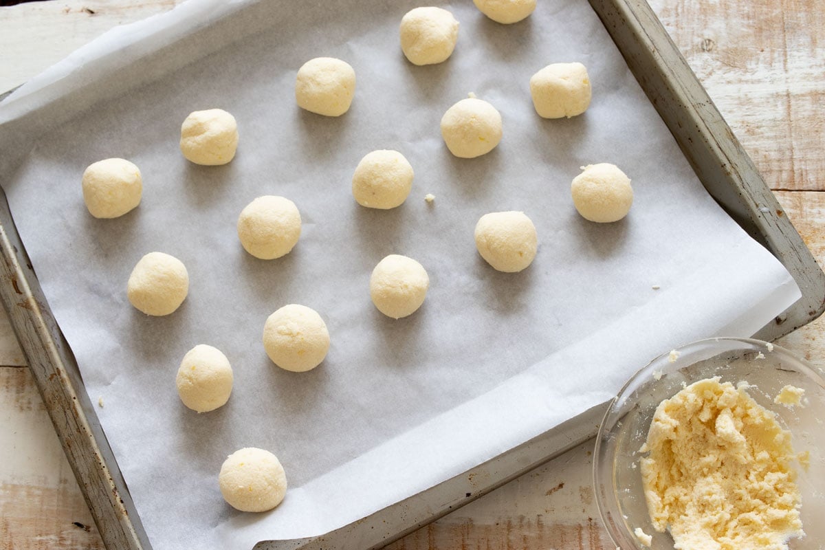 Cookie dough balls on a cookie sheet and a bowl with cookie dough.