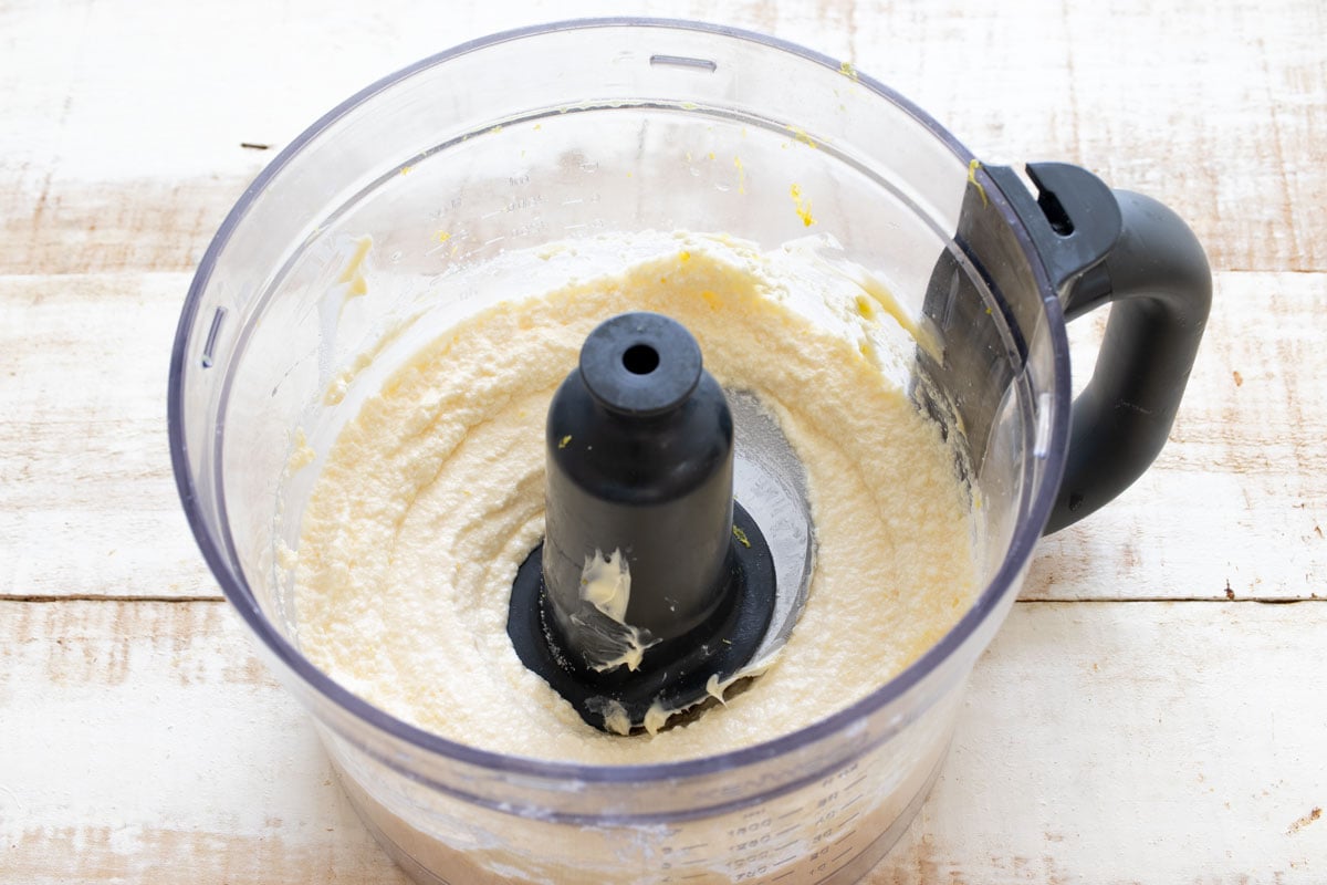 Blended wet ingredients in a food processor bowl, including the cottage cheese, now smooth.