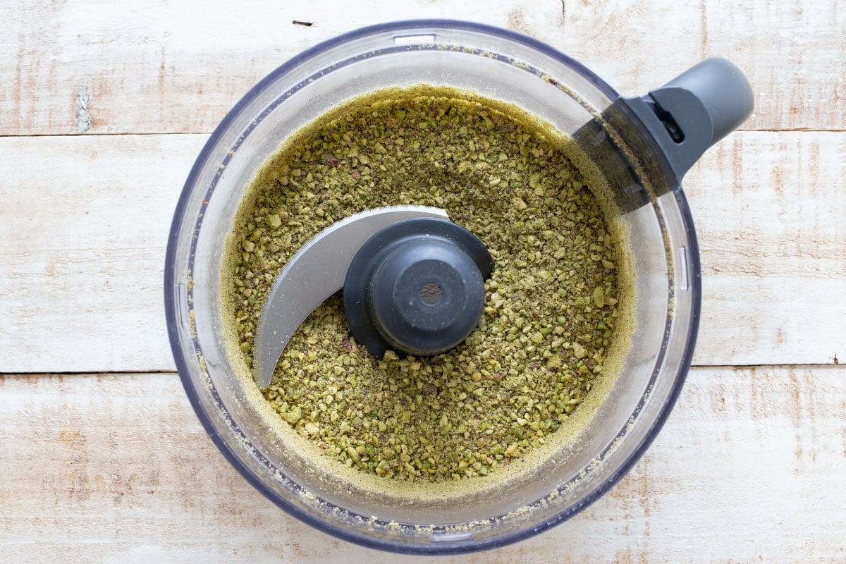 Ground pistachios in a foor processor bowl with larger and smaller pieces.