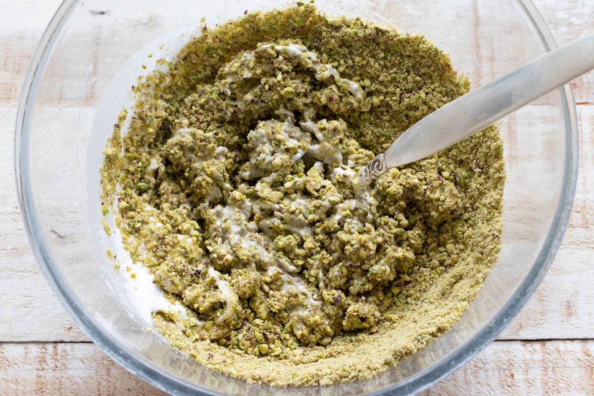 Mixing the ground pistachios into the egg white sweetener mixture with a fork.