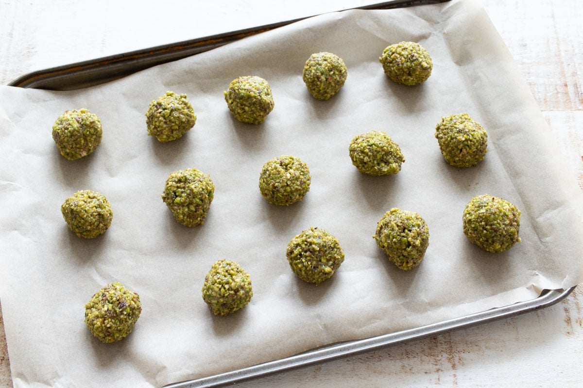 Pistachio cookie dough balls on a baking sheet lined with parchment paper.